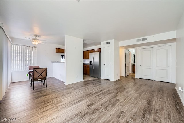 unfurnished living room featuring a ceiling fan, visible vents, baseboards, and wood finished floors