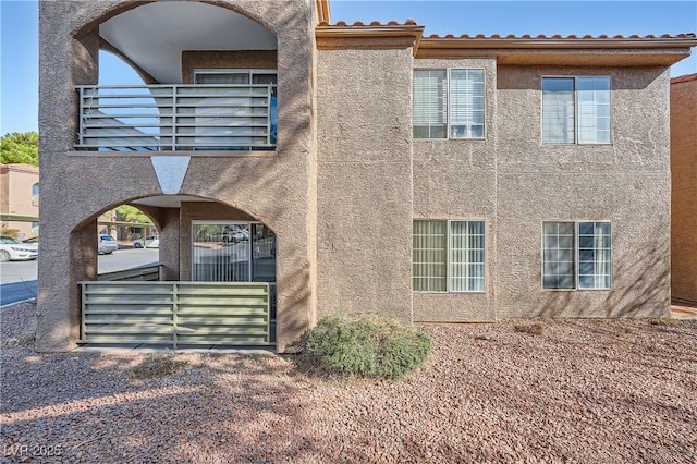 exterior space featuring a balcony, a tiled roof, and stucco siding