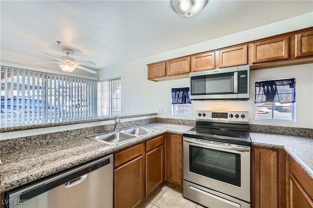 kitchen featuring brown cabinets, appliances with stainless steel finishes, a ceiling fan, light tile patterned flooring, and a sink