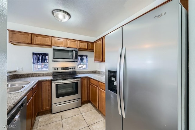 kitchen featuring appliances with stainless steel finishes, brown cabinets, a sink, and light tile patterned flooring