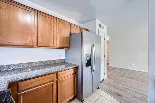 kitchen featuring light tile patterned floors, visible vents, brown cabinetry, dark stone countertops, and stainless steel refrigerator with ice dispenser