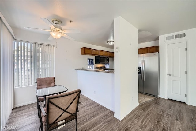 kitchen featuring visible vents, brown cabinetry, a ceiling fan, wood finished floors, and stainless steel appliances