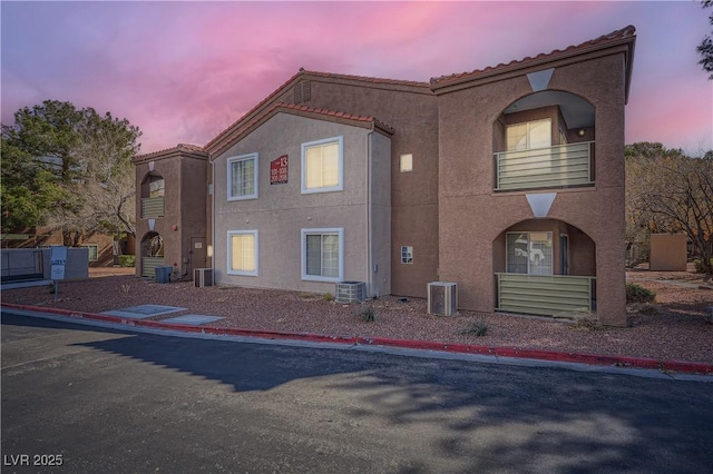 view of front of property featuring central air condition unit, a balcony, a tiled roof, and stucco siding