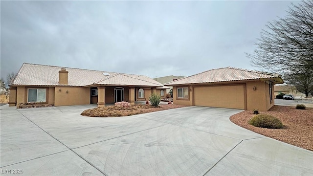 view of front of property featuring driveway, a tiled roof, a chimney, and stucco siding