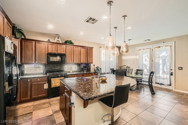 kitchen featuring visible vents, black appliances, a breakfast bar, a sink, and tasteful backsplash