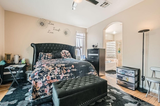 bedroom with visible vents, arched walkways, ensuite bath, and wood finished floors