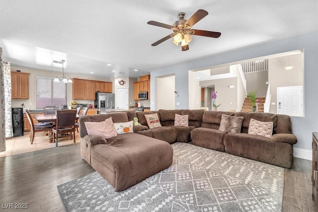 living area featuring ceiling fan with notable chandelier, light wood-style flooring, and baseboards