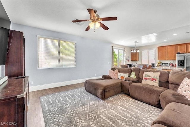 living room with light wood-style floors, recessed lighting, baseboards, and ceiling fan with notable chandelier