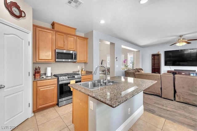 kitchen featuring light tile patterned flooring, a kitchen island with sink, a sink, visible vents, and appliances with stainless steel finishes