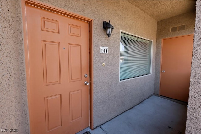 property entrance with visible vents and stucco siding