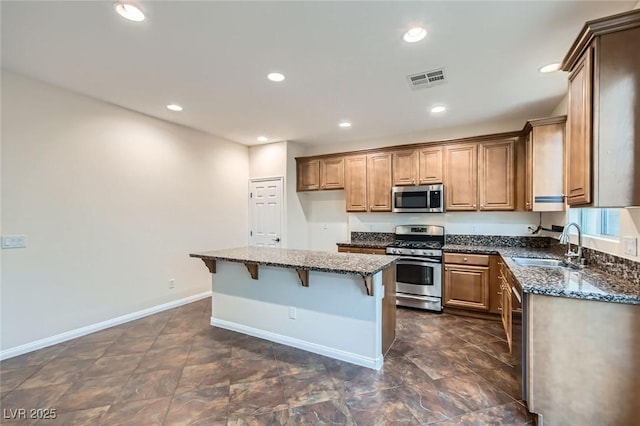 kitchen with appliances with stainless steel finishes, a breakfast bar area, dark stone countertops, and a sink