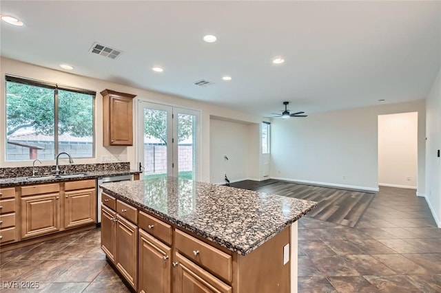 kitchen featuring a kitchen island, visible vents, dark stone counters, and a sink