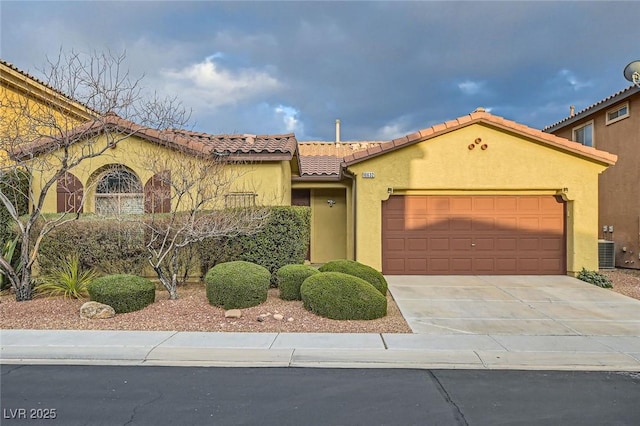 mediterranean / spanish home featuring driveway, an attached garage, a tiled roof, and stucco siding