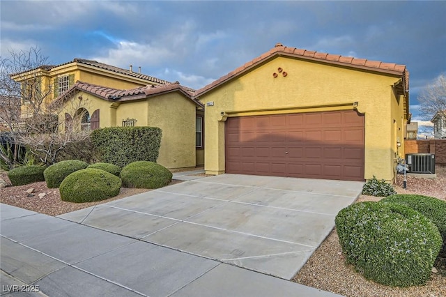 mediterranean / spanish home featuring concrete driveway, central AC, an attached garage, and stucco siding