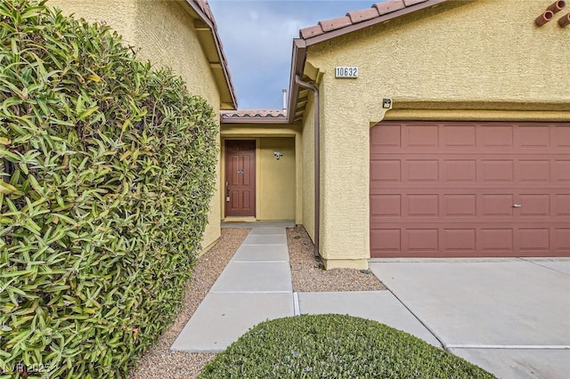 doorway to property with a tiled roof, an attached garage, and stucco siding