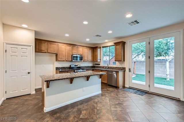 kitchen with dark stone counters, stainless steel appliances, a kitchen island, and visible vents