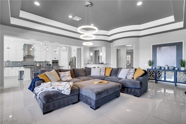 living room with an inviting chandelier, visible vents, a tray ceiling, and light tile patterned flooring