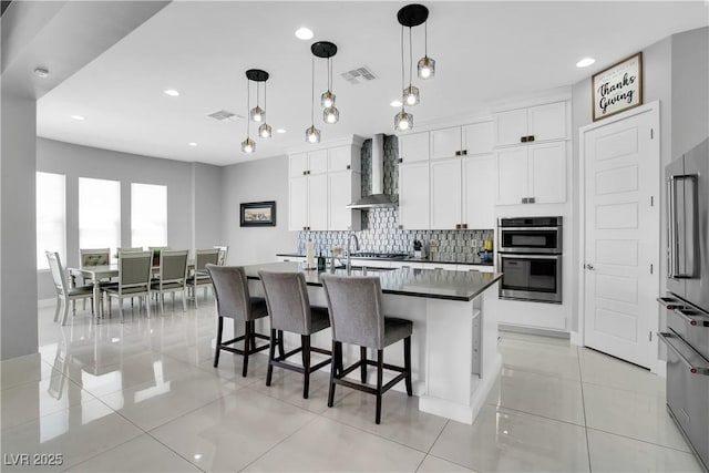 kitchen featuring a kitchen bar, visible vents, backsplash, appliances with stainless steel finishes, and wall chimney exhaust hood