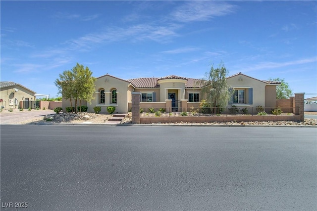 mediterranean / spanish-style home with a fenced front yard, a tiled roof, and stucco siding