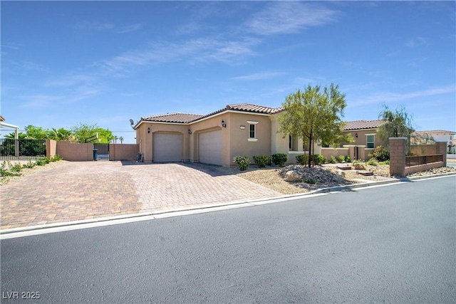 mediterranean / spanish-style home with a garage, a tiled roof, a gate, fence, and decorative driveway