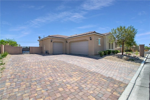 mediterranean / spanish-style house featuring a garage, a tile roof, a gate, decorative driveway, and stucco siding