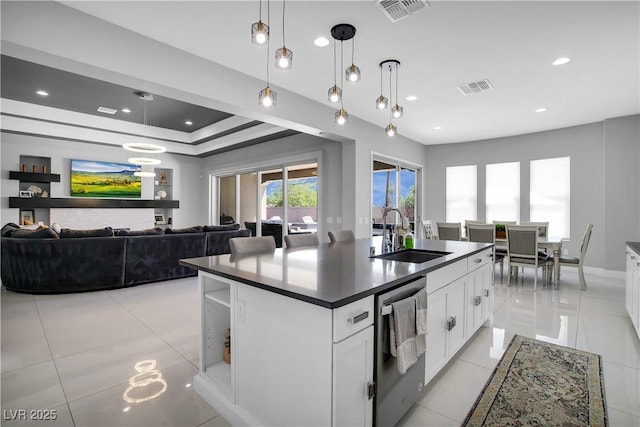 kitchen featuring stainless steel dishwasher, dark countertops, a sink, and visible vents