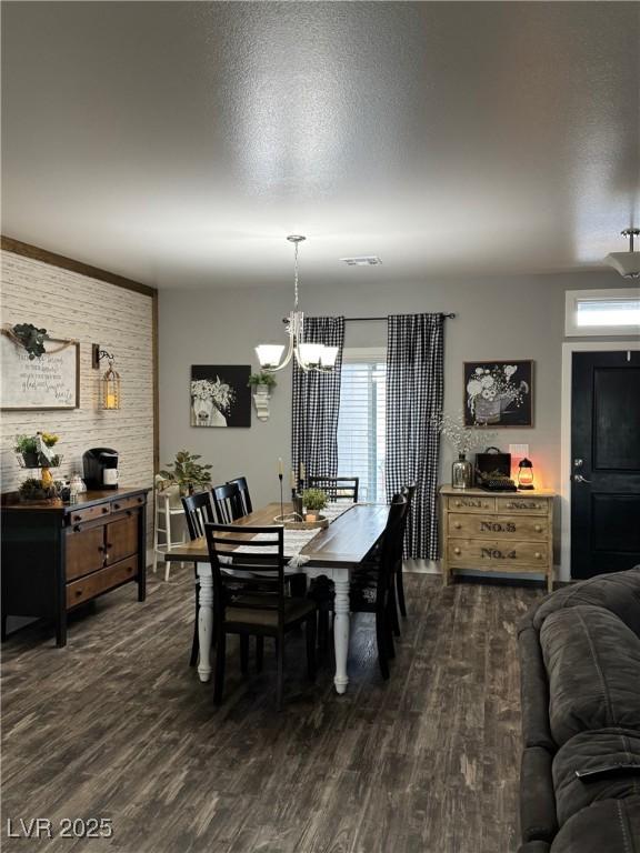 dining space with a textured ceiling, dark wood-style flooring, visible vents, and an inviting chandelier