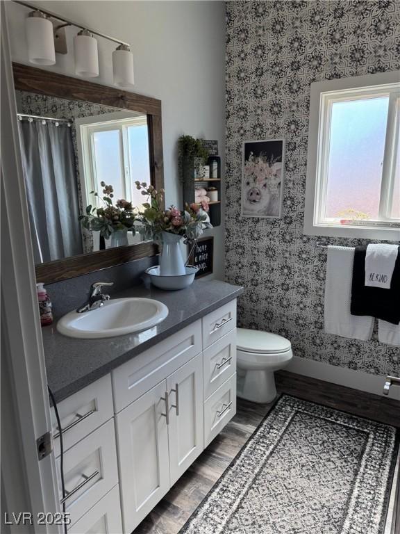 full bathroom featuring toilet, wood finished floors, vanity, and wallpapered walls