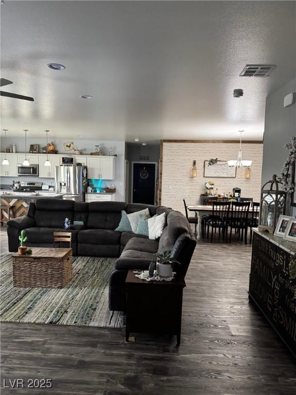 living area with dark wood-style flooring, visible vents, a textured ceiling, and an inviting chandelier