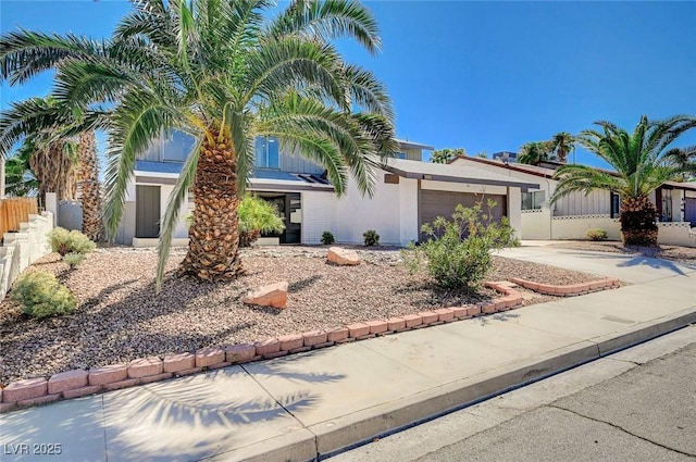 view of front of property with driveway, an attached garage, fence, and stucco siding