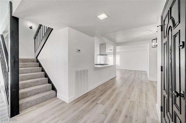 foyer entrance featuring visible vents, stairway, light wood-style flooring, a textured ceiling, and baseboards