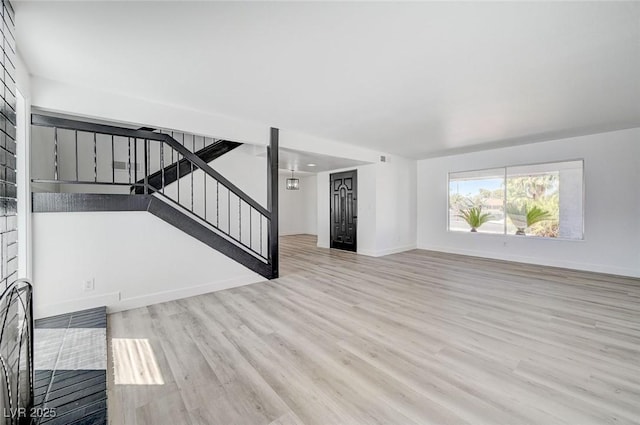 unfurnished living room with stairs, wood finished floors, and baseboards