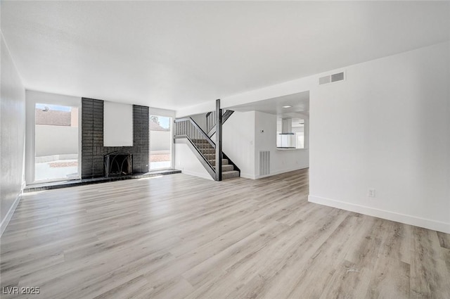 unfurnished living room with visible vents, baseboards, light wood-style floors, stairway, and a brick fireplace