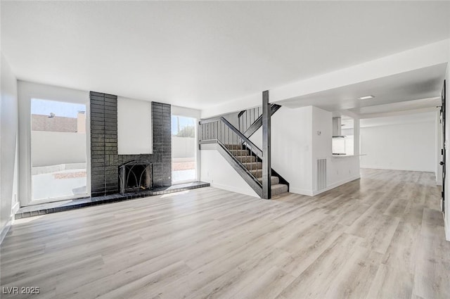 unfurnished living room with light wood-type flooring, a brick fireplace, stairs, and baseboards