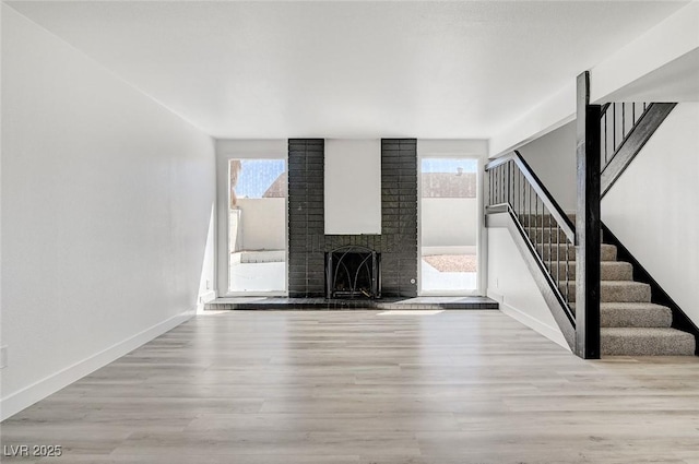 unfurnished living room featuring a wealth of natural light, wood finished floors, a fireplace, and stairs