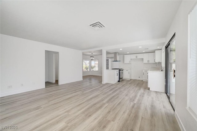 unfurnished living room with a notable chandelier, a sink, visible vents, baseboards, and light wood-style floors