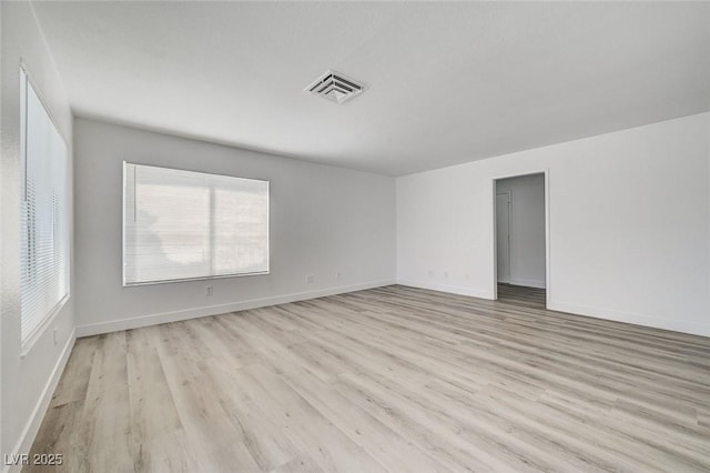 empty room featuring plenty of natural light, light wood-style flooring, visible vents, and baseboards