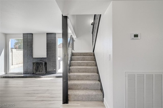 stairs with baseboards, a fireplace, visible vents, and wood finished floors