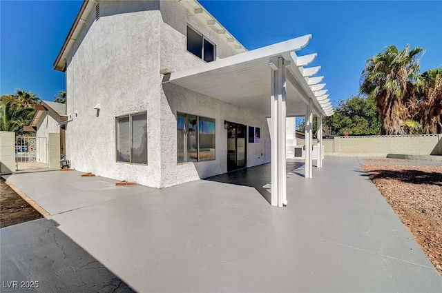 rear view of property featuring a gate, a patio area, fence, and stucco siding