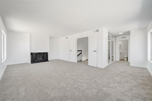 unfurnished living room with carpet floors, a fireplace with flush hearth, visible vents, and baseboards