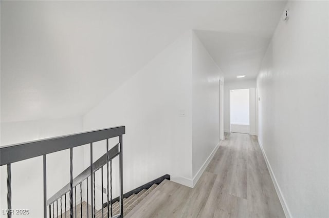 corridor featuring light wood finished floors, baseboards, and an upstairs landing