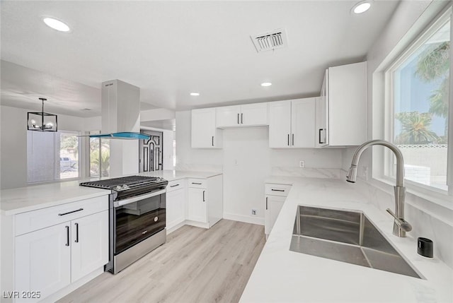 kitchen with island exhaust hood, visible vents, stainless steel range with gas stovetop, a sink, and light wood-type flooring