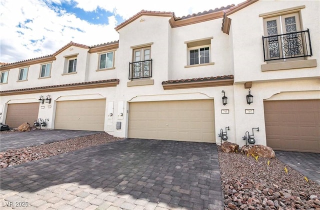 mediterranean / spanish house featuring a garage, decorative driveway, a balcony, and stucco siding