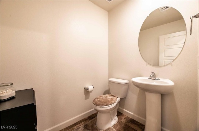 bathroom featuring visible vents, baseboards, toilet, tile patterned floors, and a sink