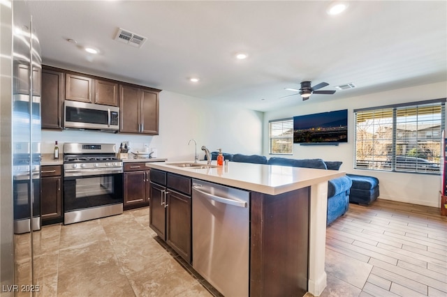 kitchen with a sink, open floor plan, light countertops, appliances with stainless steel finishes, and dark brown cabinets