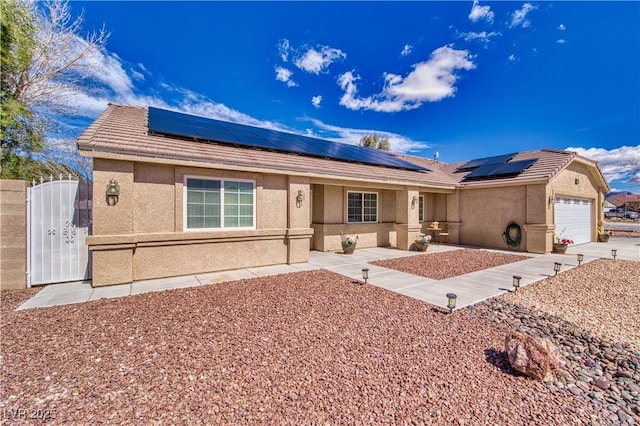 ranch-style home featuring stucco siding, a tile roof, a gate, an attached garage, and solar panels