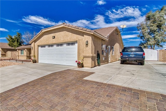 view of home's exterior with stucco siding, a gate, a tile roof, concrete driveway, and a garage