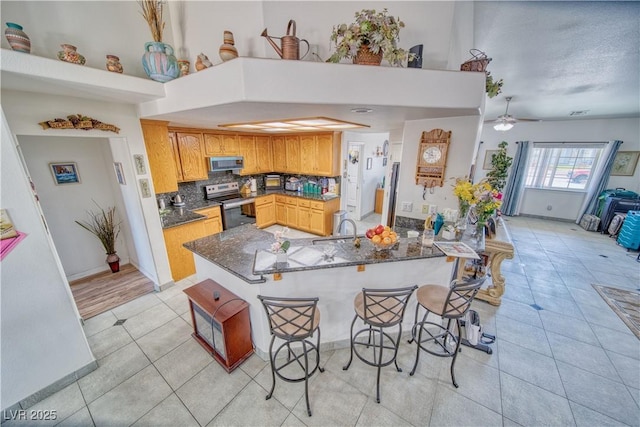 kitchen with dark stone countertops, a peninsula, light tile patterned flooring, decorative backsplash, and appliances with stainless steel finishes