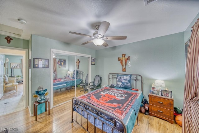 bedroom featuring a ceiling fan, light wood finished floors, attic access, a closet, and a textured ceiling