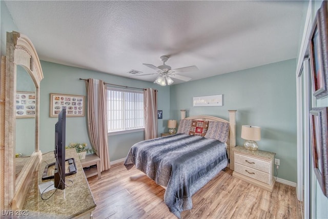 bedroom featuring light wood finished floors, visible vents, a textured ceiling, and baseboards